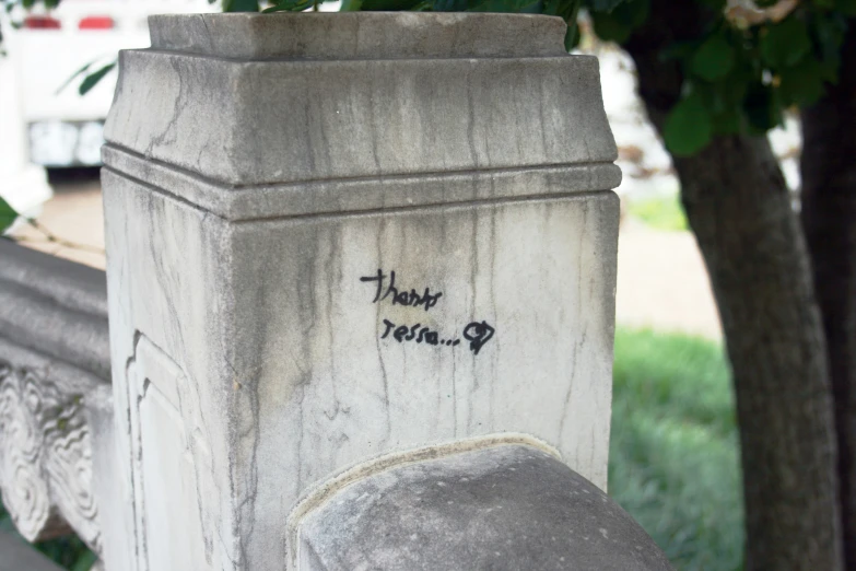 graffiti written on a white wall near a bush