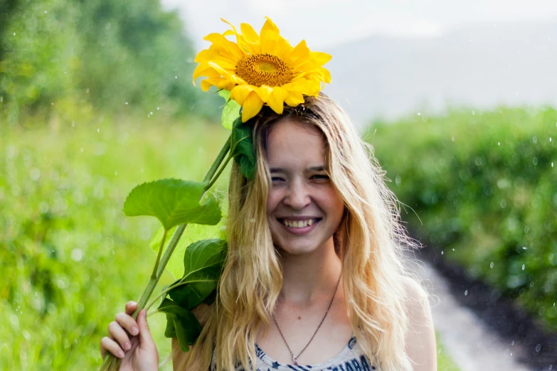 a woman with a sunflower in her hair stands by the road and holds a stalk