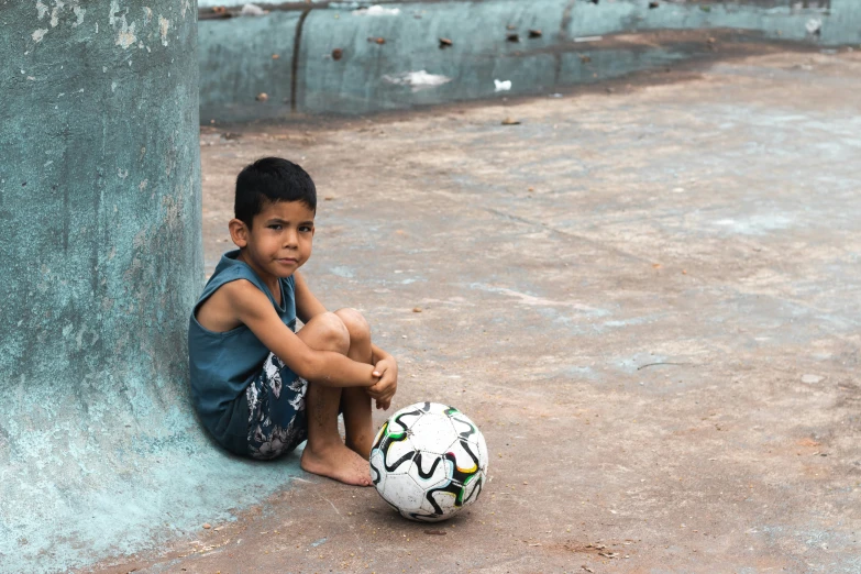 a little boy sitting next to a pole with a soccer ball