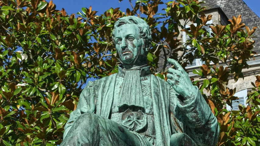 the bronze statue of a person is near the green leaves