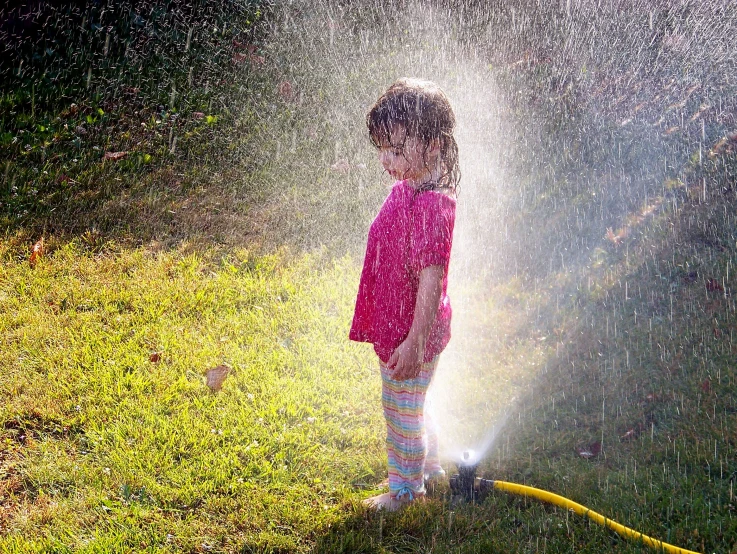 a girl spraying water with an umbrella and hose in the backyard