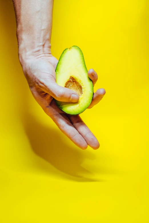 a person's hand holding an avocado slice with other half