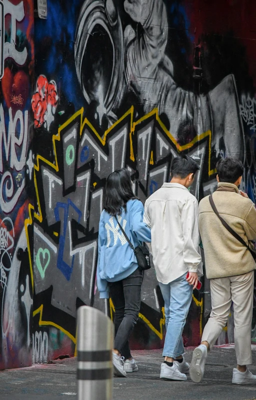 people walking in front of a wall with graffiti on it