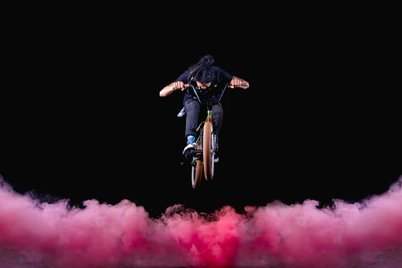 a man jumps over pink smoke on his bike