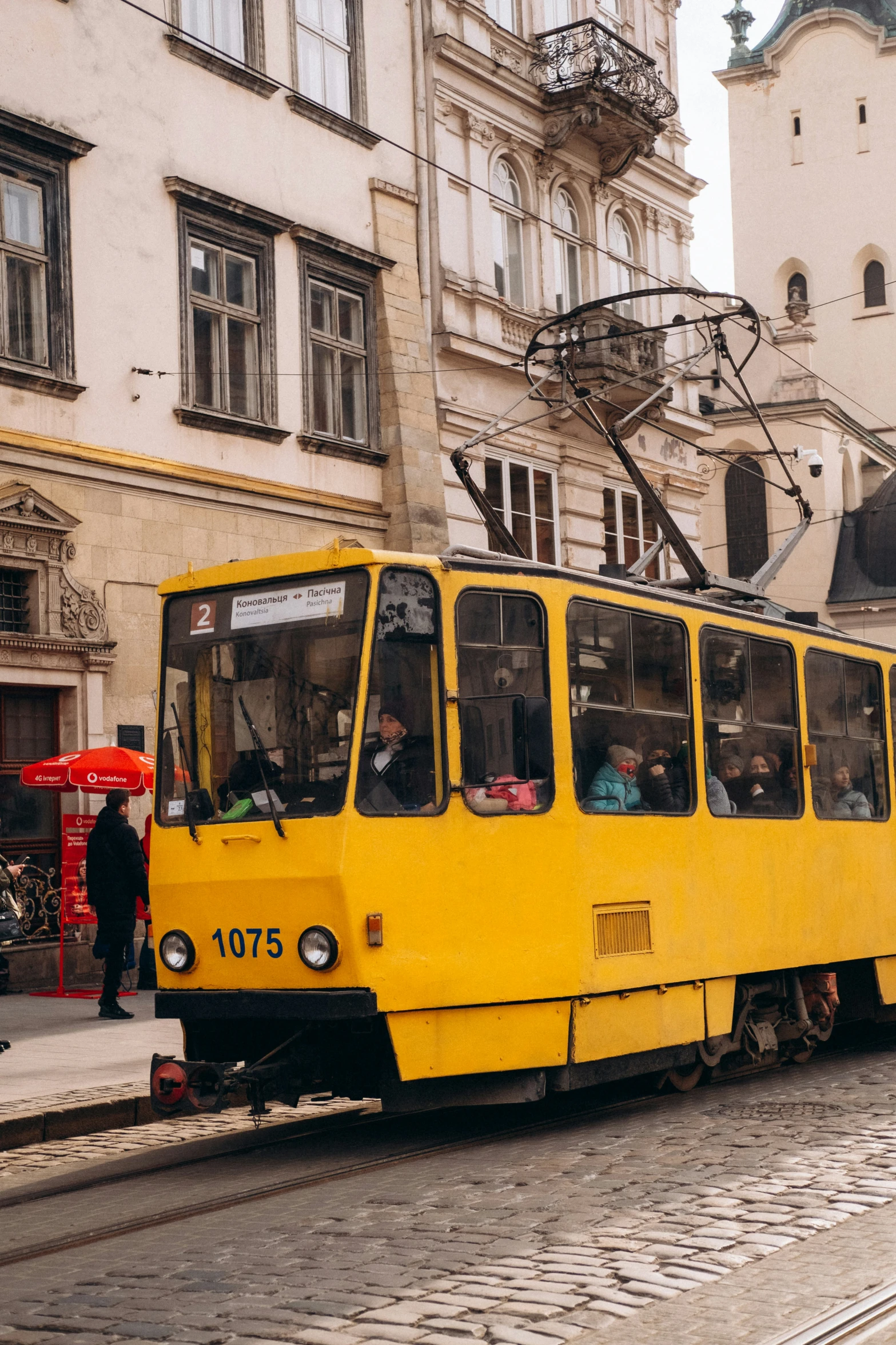 people are aboard a yellow trolley on a brick sidewalk