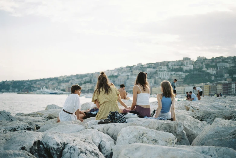 a group of people are sitting on some rocks at the water