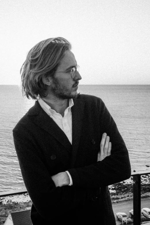 a man with glasses, standing on the balcony of a building by the ocean