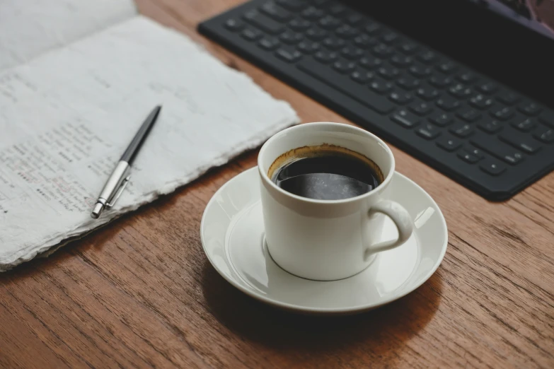 a cup of coffee sits on the table next to a computer keyboard