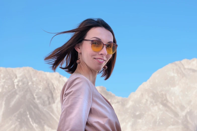 a young woman with glasses smiles against a backdrop of snowy mountains