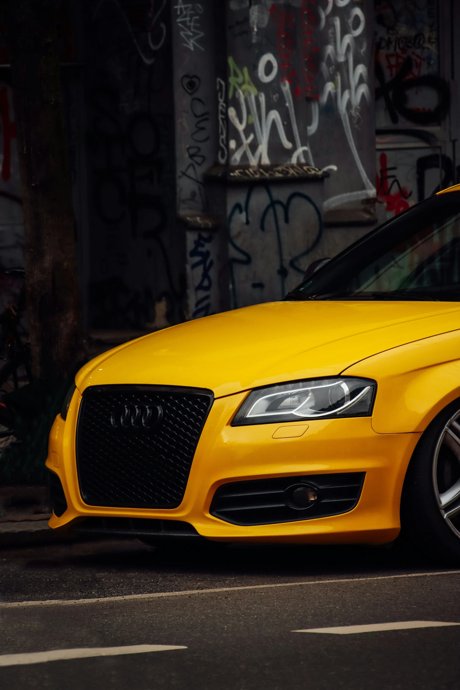 a bright yellow car is parked next to a graffiti covered wall