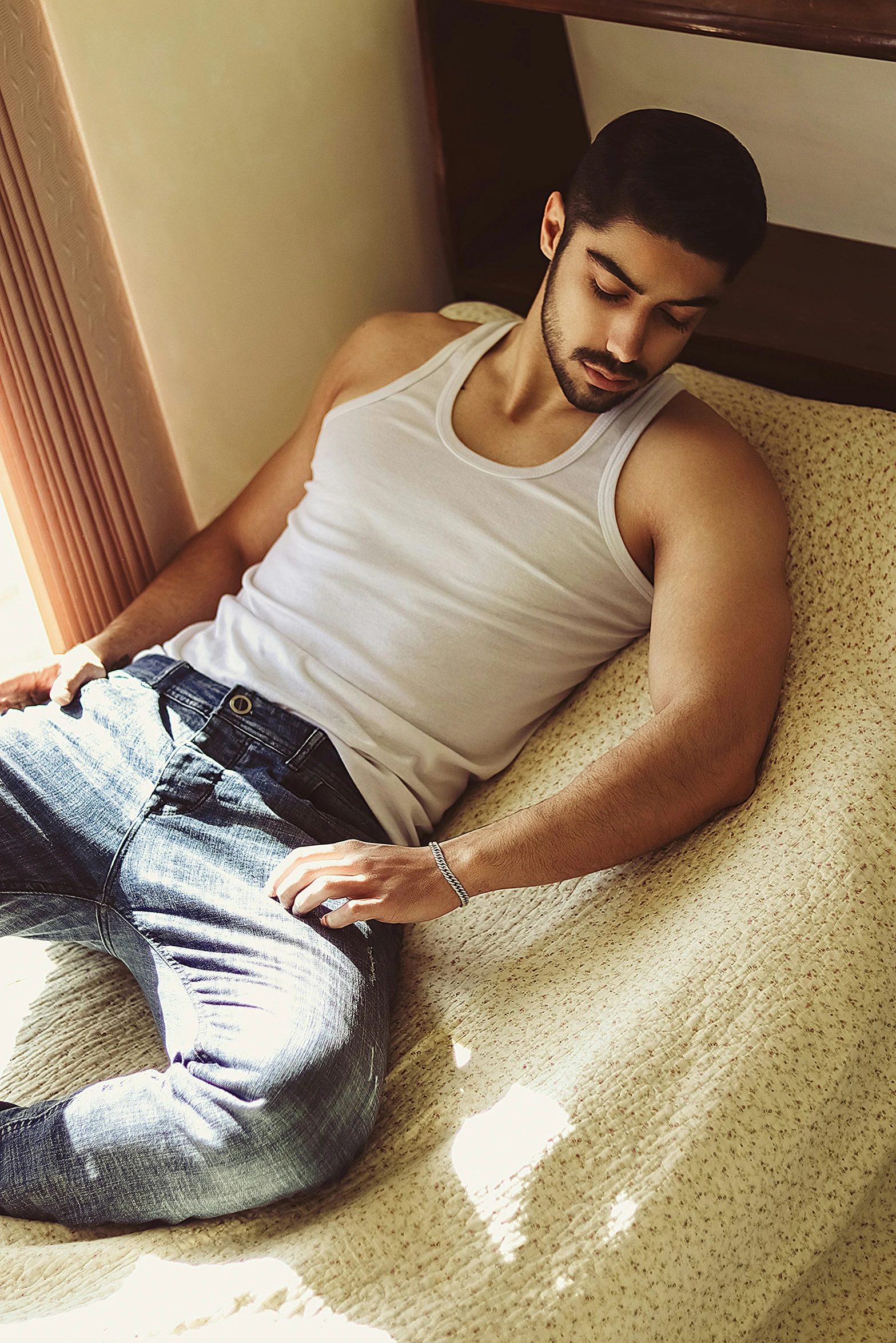 a man laying on a bed wearing blue jeans and looking at his cell phone