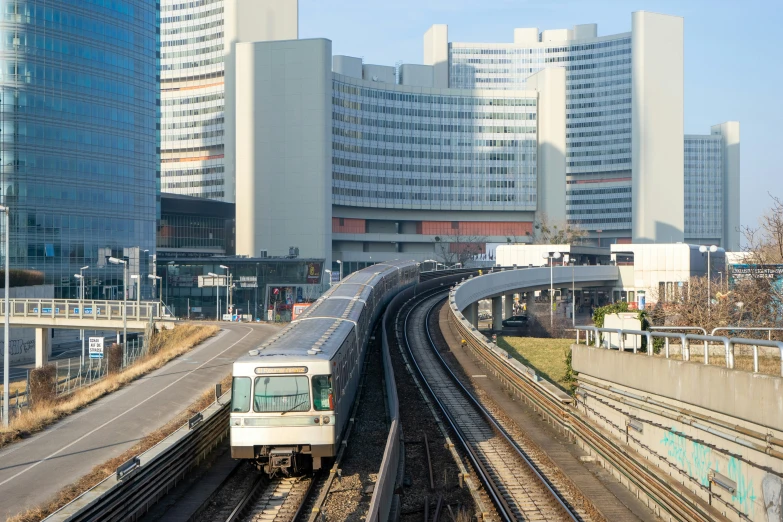 a passenger train traveling past large buildings and tracks