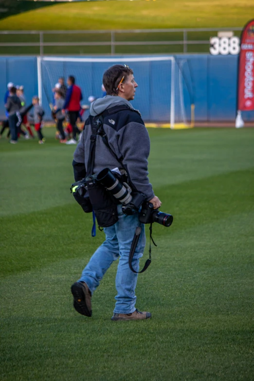 a man walking across a field with a camera in his hand