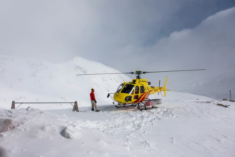 man standing next to a helicopter on the side of a snow covered mountain