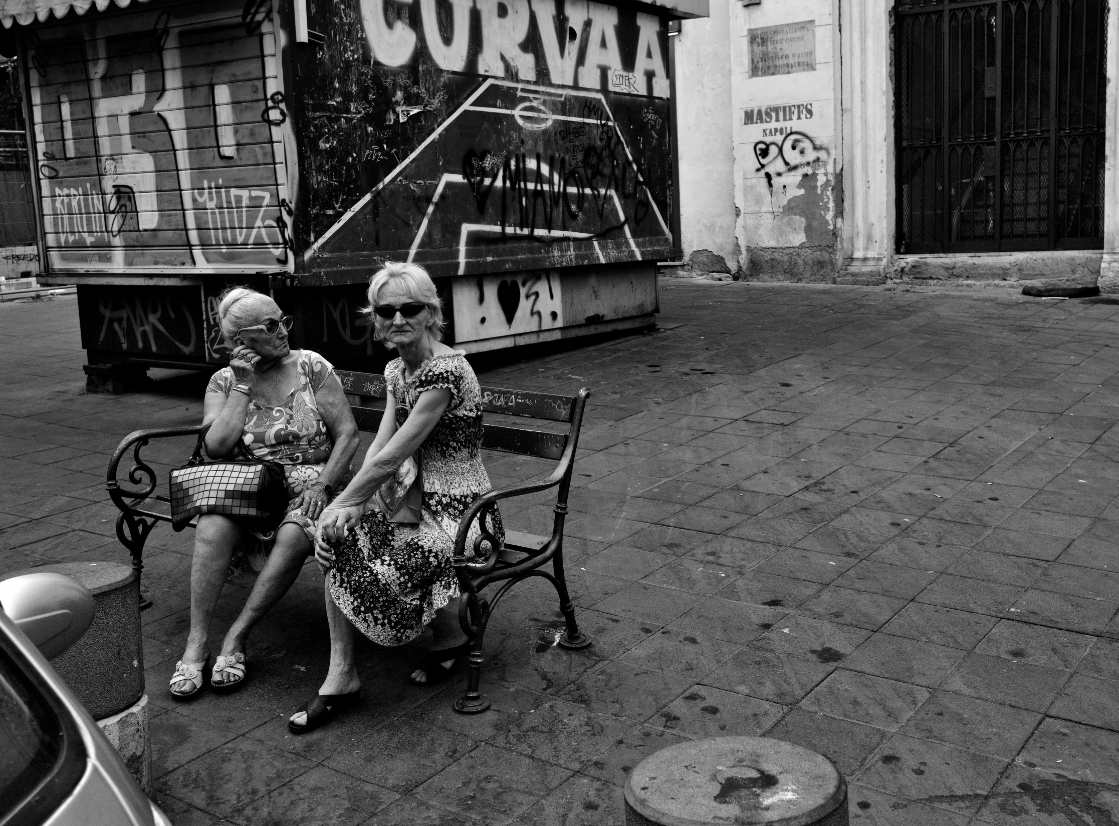 two elderly women sitting on a bench near a sign