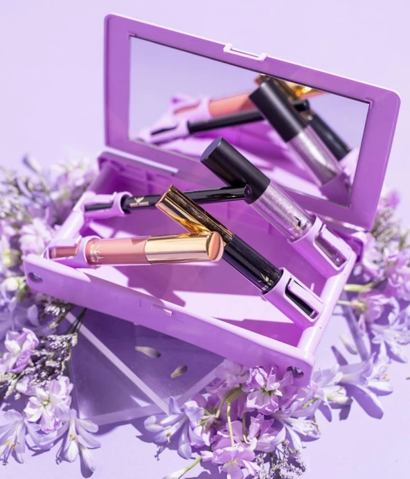 three makeup products are in an open case on a flowery purple surface