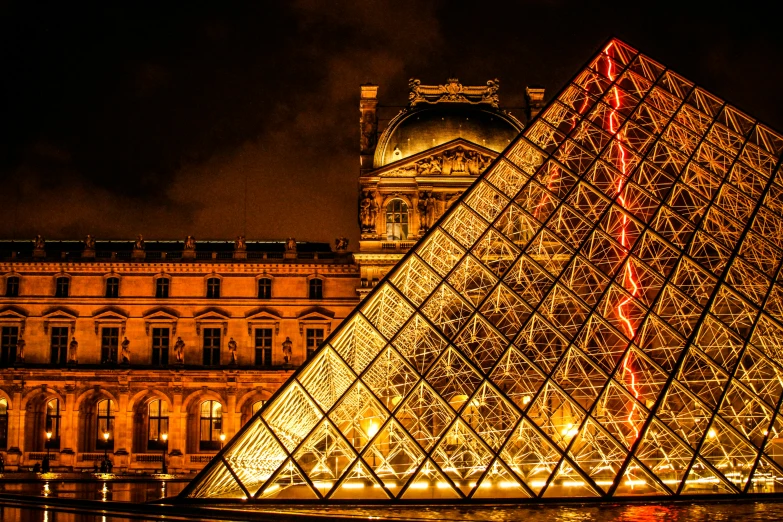 a large pyramid building in front of a building with lights on it