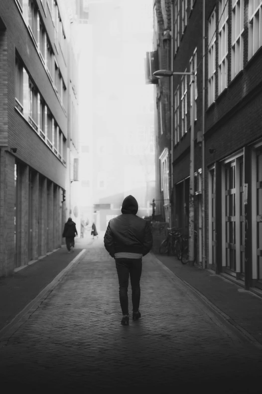 black and white pograph of person walking in alley between two buildings