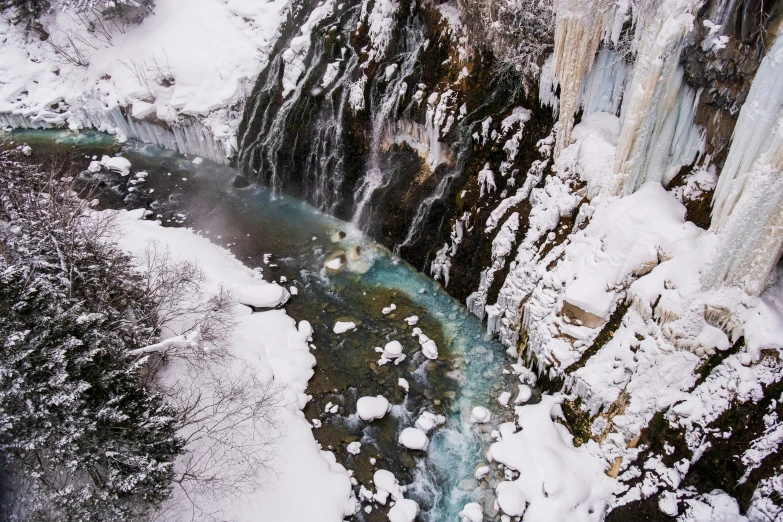 snow covers the rocks and trees at the bottom of a waterfall