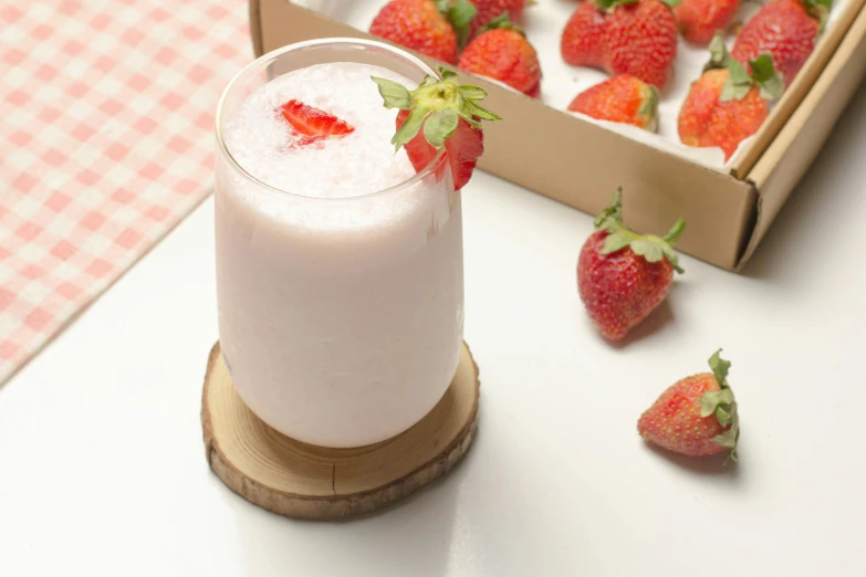 a glass of milk and strawberries next to a box of more strawberries