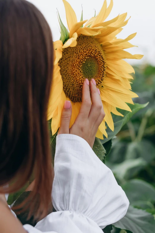 a woman in white shirt standing next to large sunflower