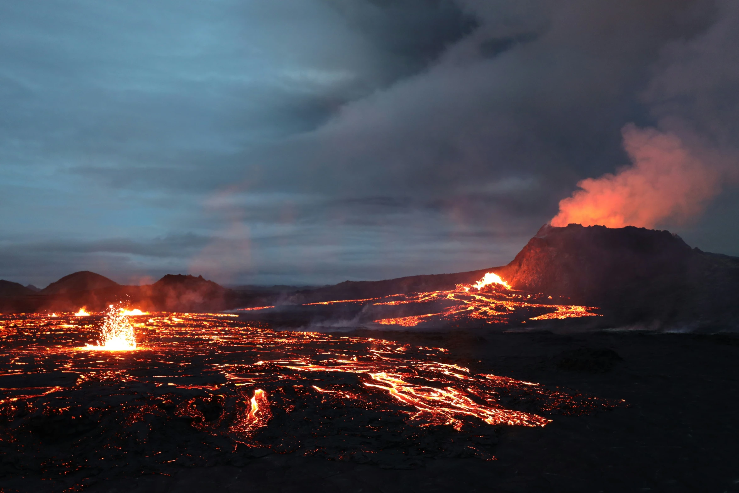 a group of lava cliffs glowing in a blue and cloudy sky