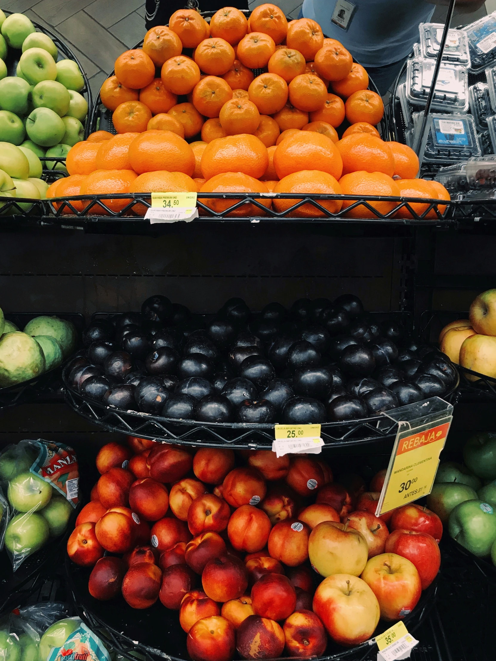 three shelves displaying various fruit including apples, tomatoes and oranges