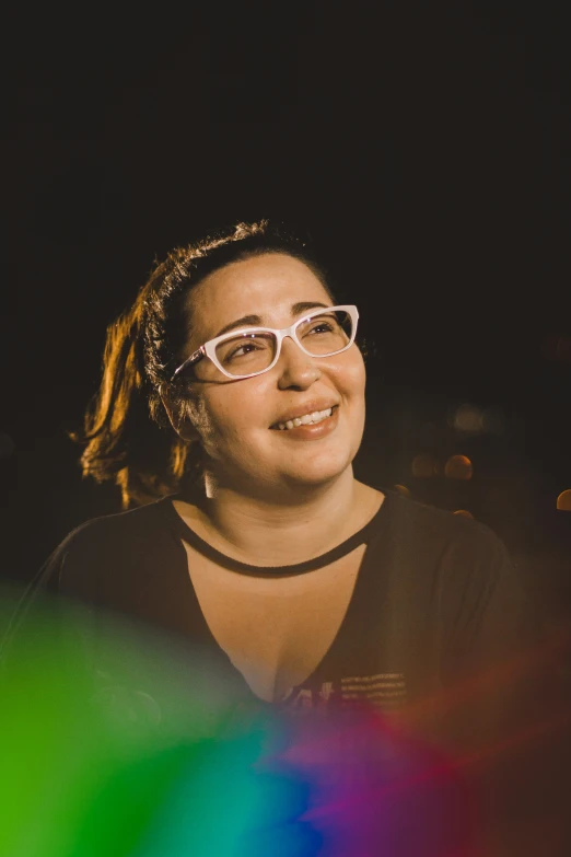 a smiling woman in glasses sits looking up