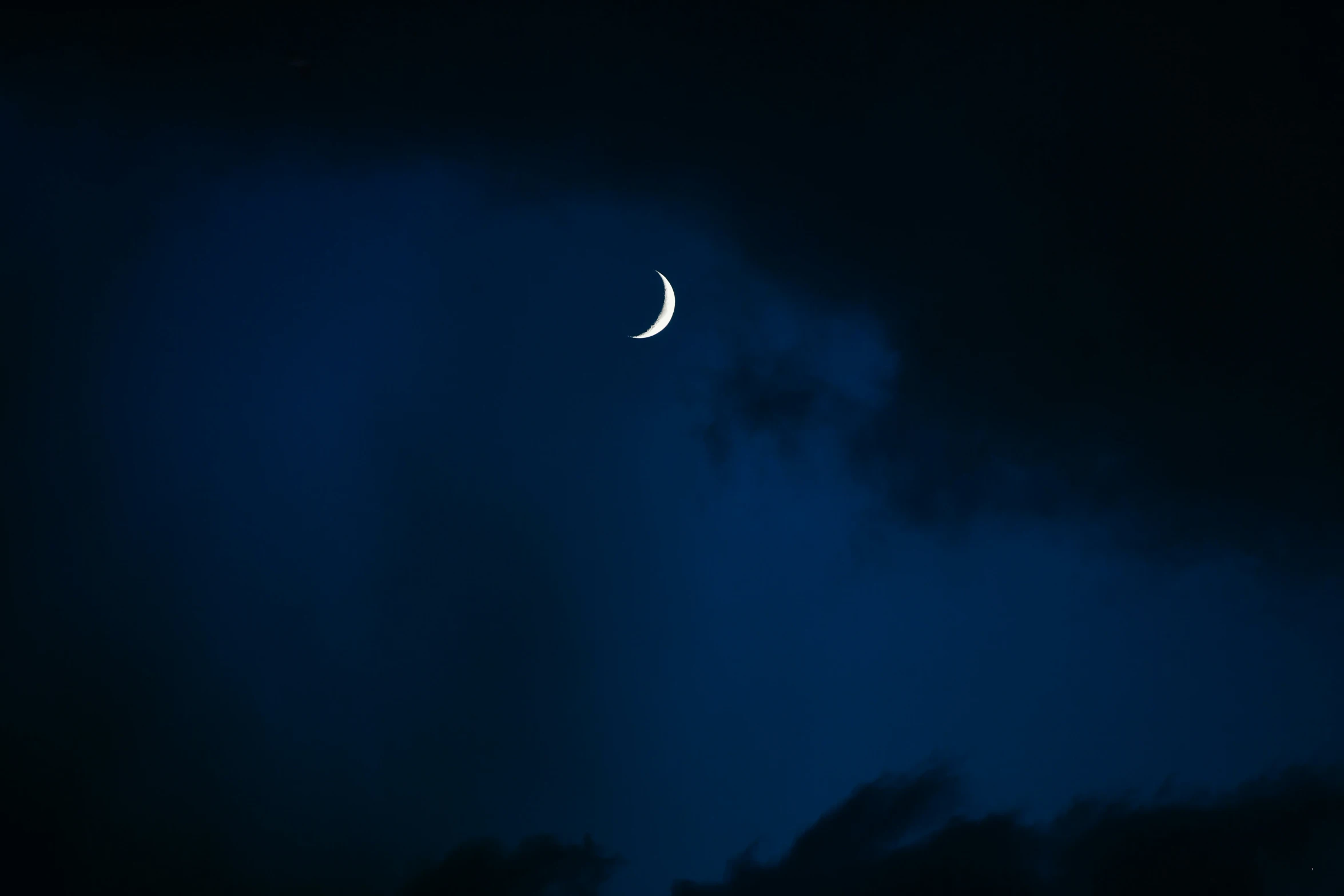 a crescent is visible at night in a cloudy sky