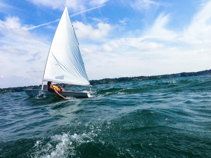 the man is out in the water on his small sail boat