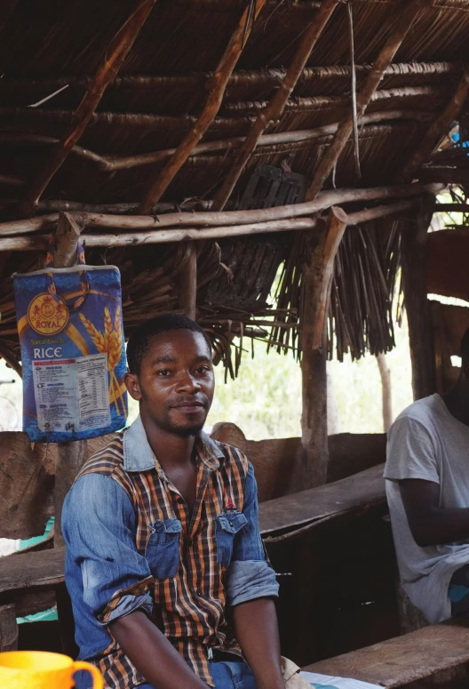 two men sit under straw houses on a dirt field