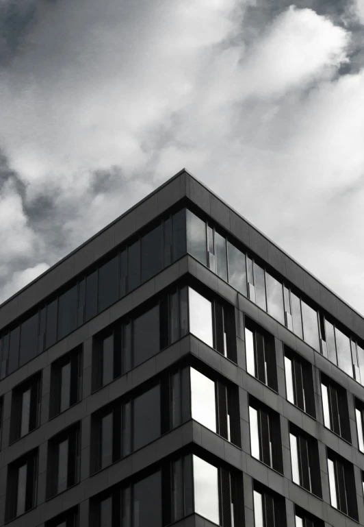 a gray building with multiple windows is in front of the cloudy sky