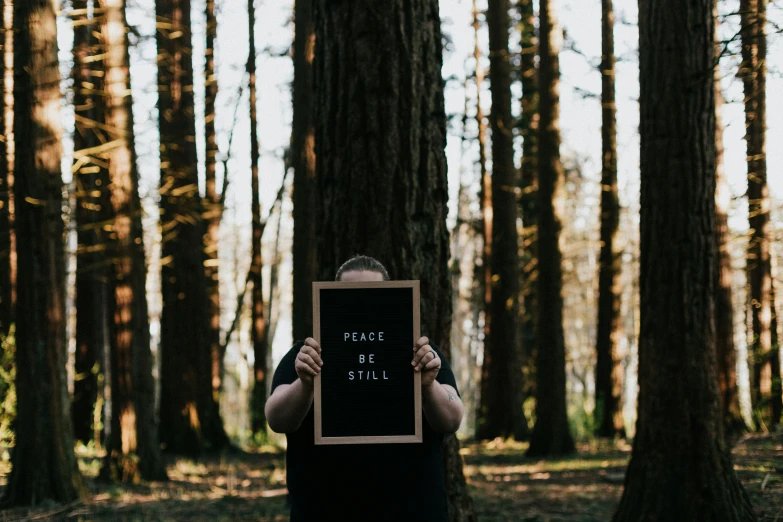 a person holding a black and white sign in the woods