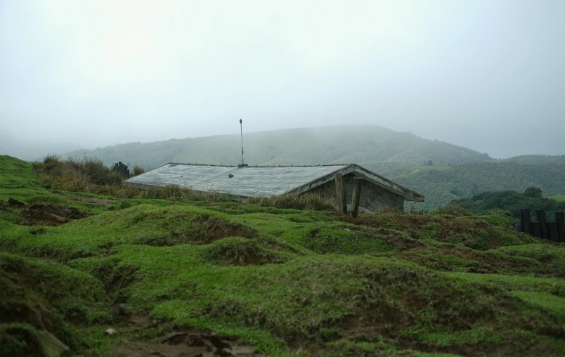 an old cabin on a grassy hill in the mist