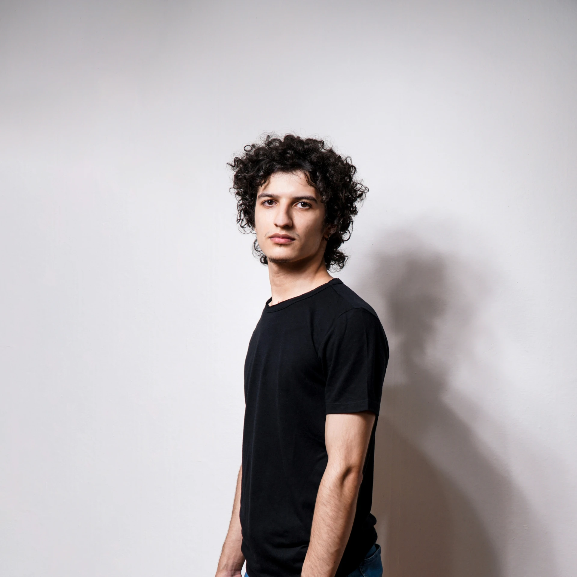 a man in black shirt and jean shorts standing by wall