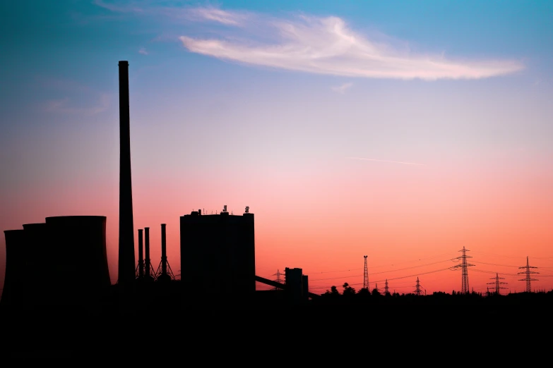 factory plant silhouetted against a sunset sky with power lines in the foreground