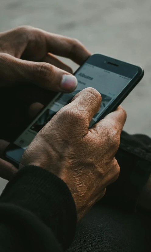 a person's hands hold a black phone in their left hand