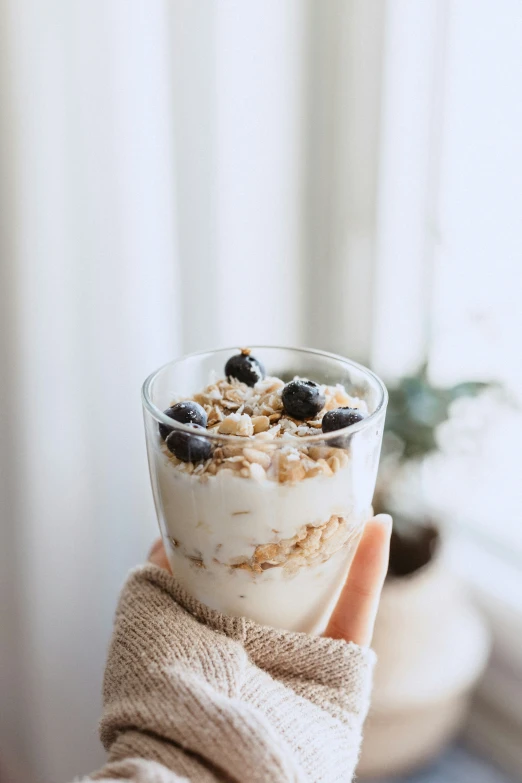 a person holding a glass of food that includes cereal