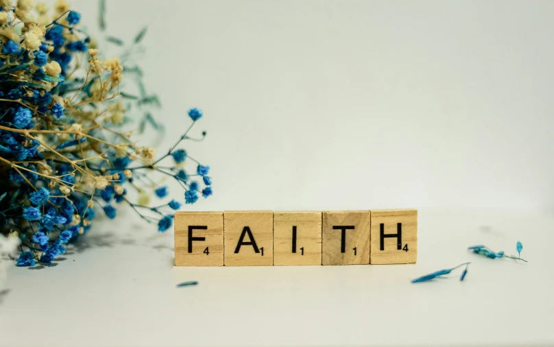 scrabble block spelling faith next to blue flowers