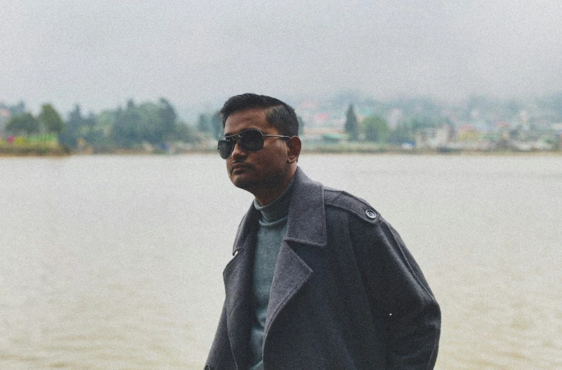 a man is standing by the water wearing sunglasses