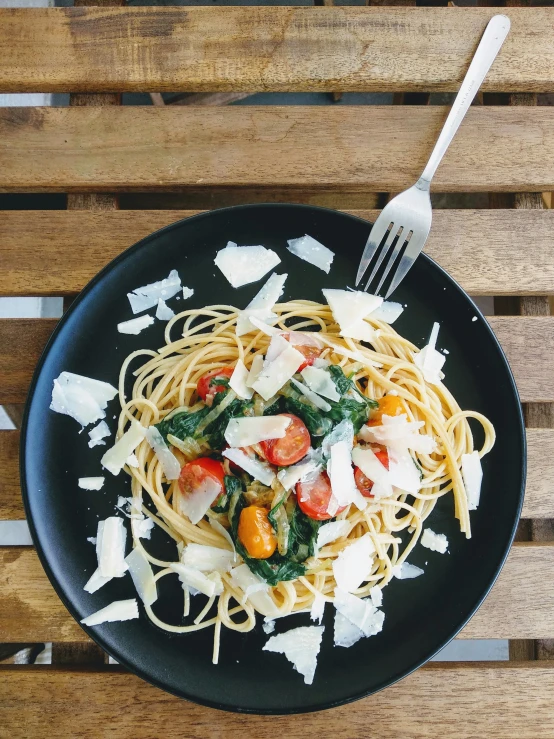 pasta with tomato, spinach and parmesan cheese on a black plate with a fork