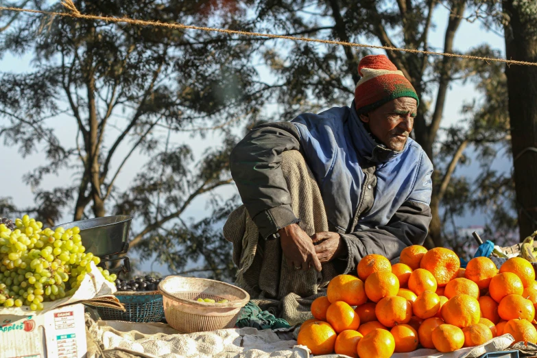 an elderly man squatting down next to a pile of oranges