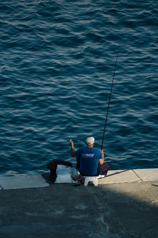 a man is sitting and fishing on the edge of a pier