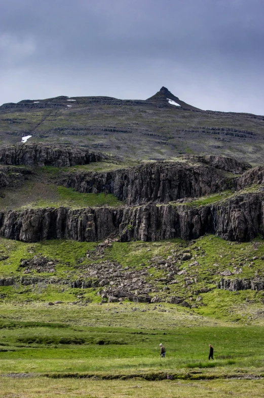 two people walking in the distance on grassy plain near hills