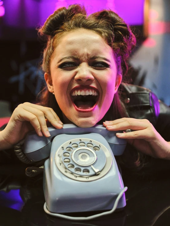 a woman has her mouth open and is holding an old style grey phone