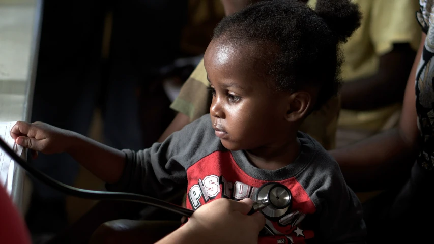 a small child holding a white stethoscope and looking at soing