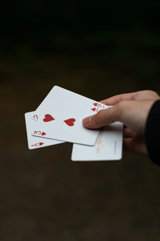 two white cards with red hearts and one hand holding another