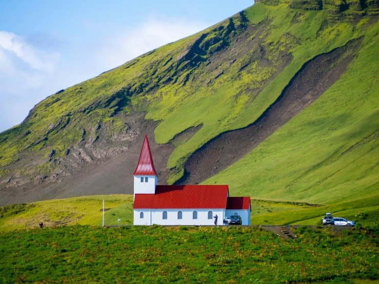 a church with red roof stands by the side of a green hill