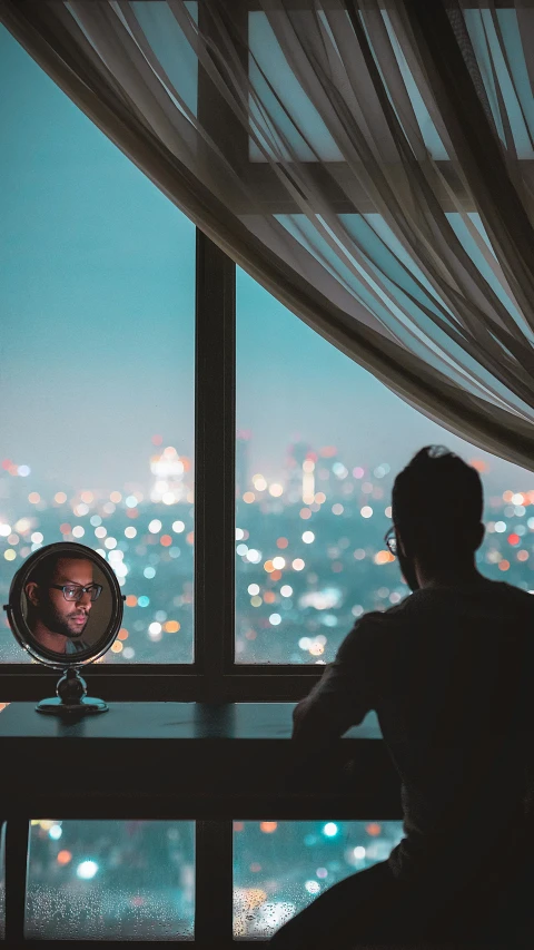 a man sitting in a room looking out at a city