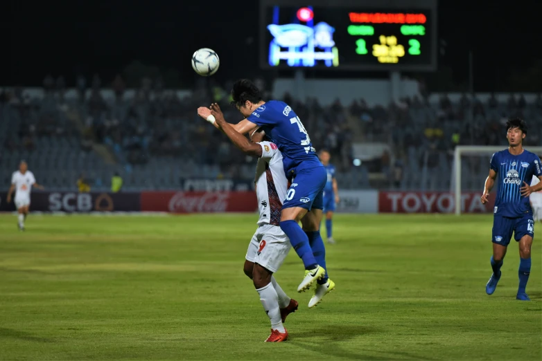 two young men playing soccer at night, jumping to head the ball